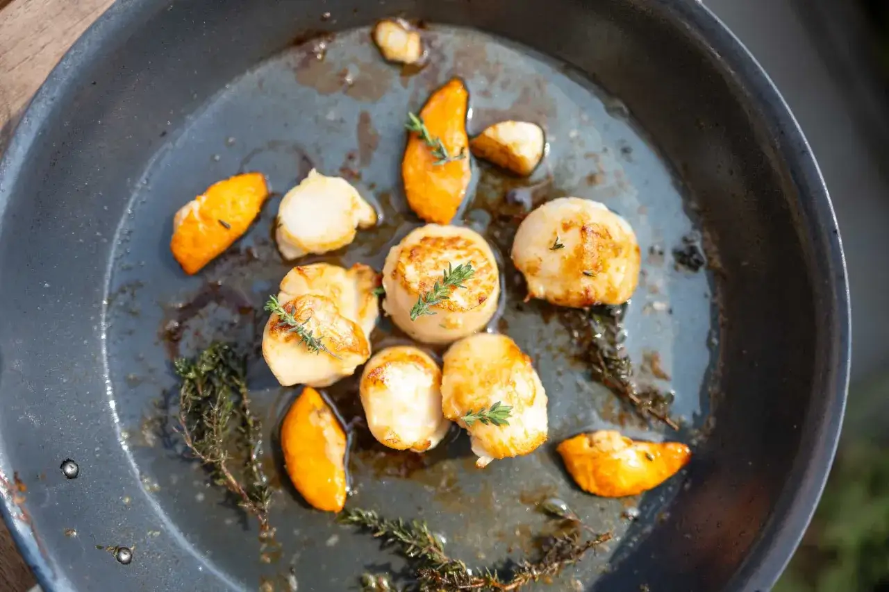 Gebratene Jakobsmuscheln mit K&uuml;rbisspalten und Thymian in einer Pfanne. Ein einfaches Jakobsmuscheln Rezept f&uuml;r Genie&szlig;er.