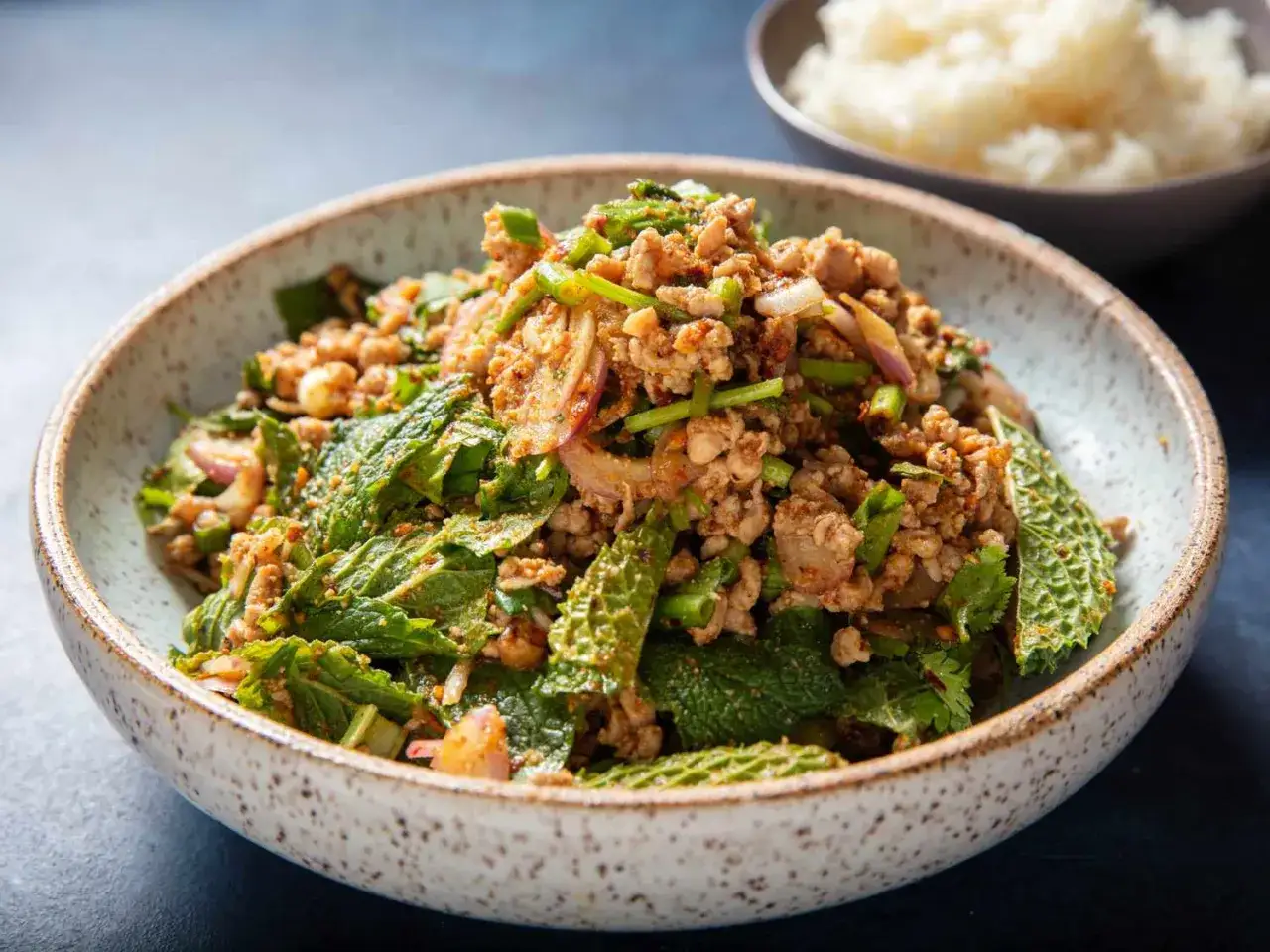 Sch&uuml;ssel mit w&uuml;rzigem Larb Moo, einem thail&auml;ndischen Hackfleischsalat mit frischer Minze, Koriander und roten Zwiebeln. Daneben eine Schale Reis.