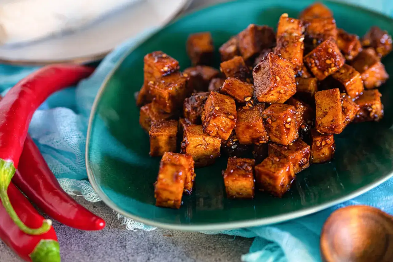 W&uuml;rzig gebratene Tofuw&uuml;rfel auf einem gr&uuml;nen Teller, daneben rote Chilis. So schmeckt Tofu!