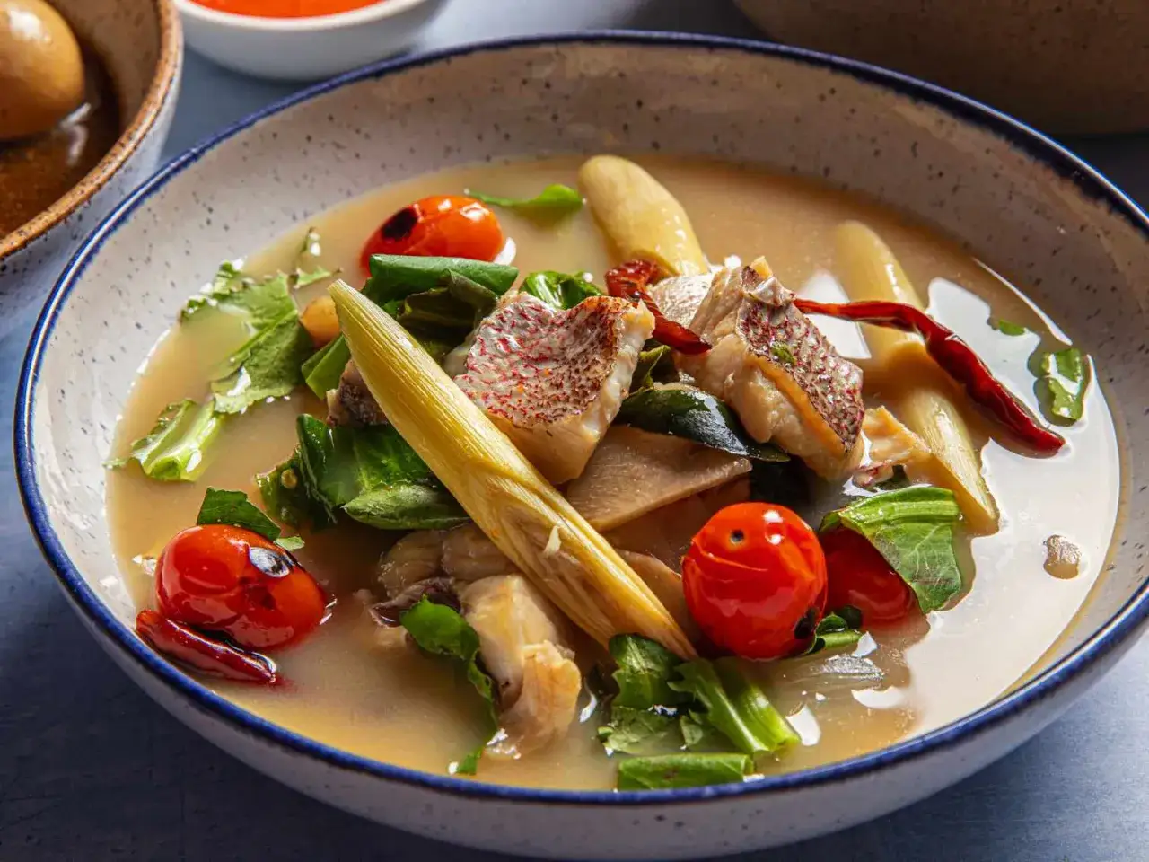 Eine dampfende Sch&uuml;ssel mit thai Fischsuppe (Tom Yum Pla) mit zarten Fischst&uuml;cken, Kirschtomaten, Zitronengras und Kr&auml;utern.
