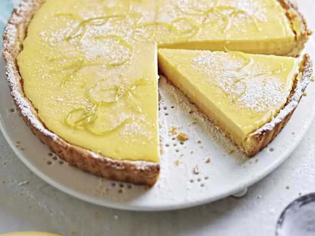 Ein Zitronen-Quatre-Quarts-Kuchen mit einem St&uuml;ck, best&auml;ubt mit Puderzucker und garniert mit Zitronenschale.