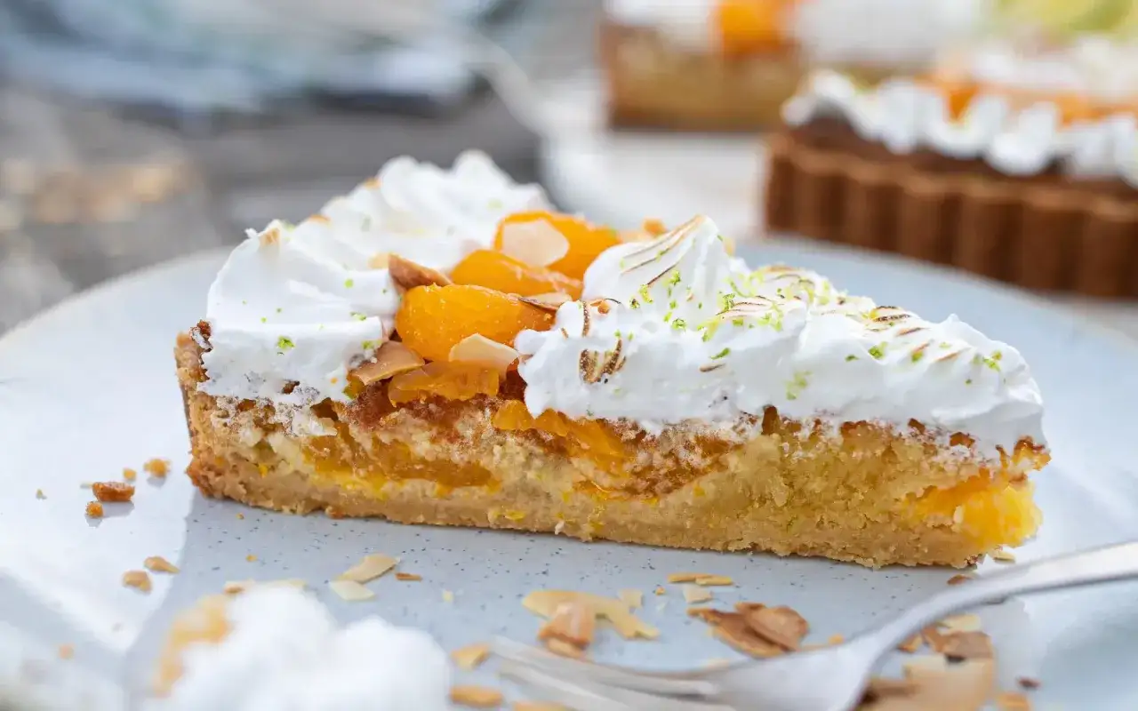 Ein St&uuml;ck Mandarinen Tarte mit Baiserhaube, Mandelsplittern und frischer Zitronenschale garniert.