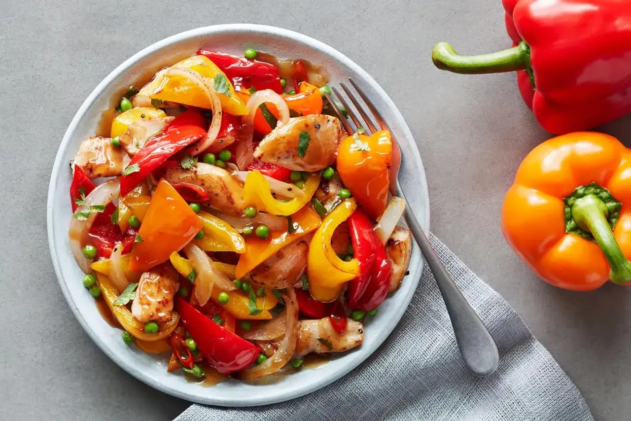 Buntes Paprika-H&auml;hnchen-Gericht mit Erbsen und Zwiebeln in einer s&uuml;&szlig;-sauren Sauce, inspiriert von asiatischer K&uuml;che.