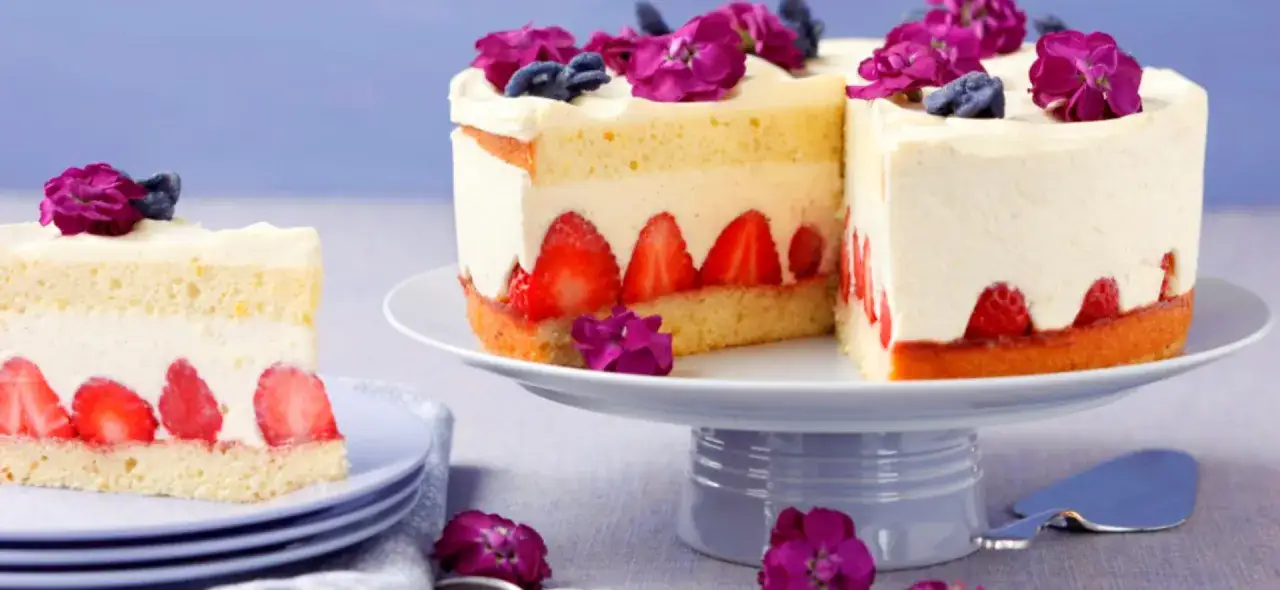 Eine köstliche Vanille Erdbeer Torte, dekoriert mit frischen Beeren und Blüten, wartet darauf, genossen zu werden.