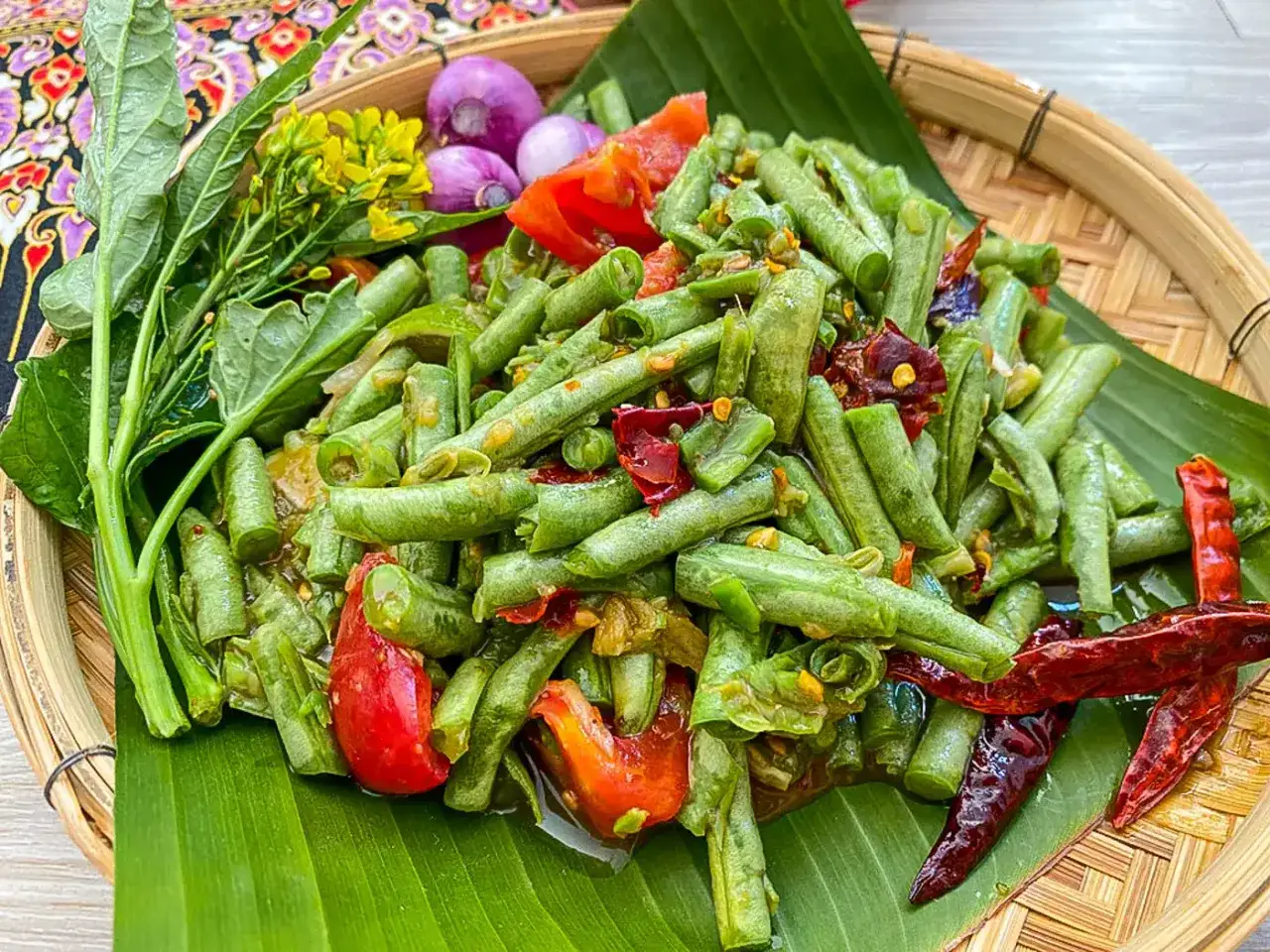 Ein w&uuml;rziger Salat aus thai bohnen mit Tomaten, Chili und Schalotten auf Bananenblatt.