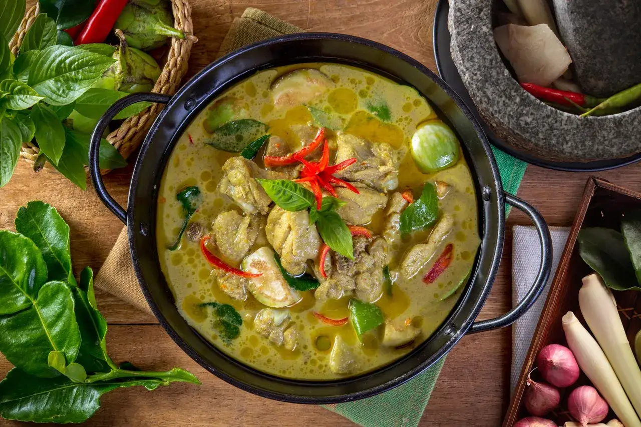Ein dampfender Topf mit Thai Green Curry, gefüllt mit Hühnchen, Auberginen und frischen Kräutern, bereit zum Genießen.
