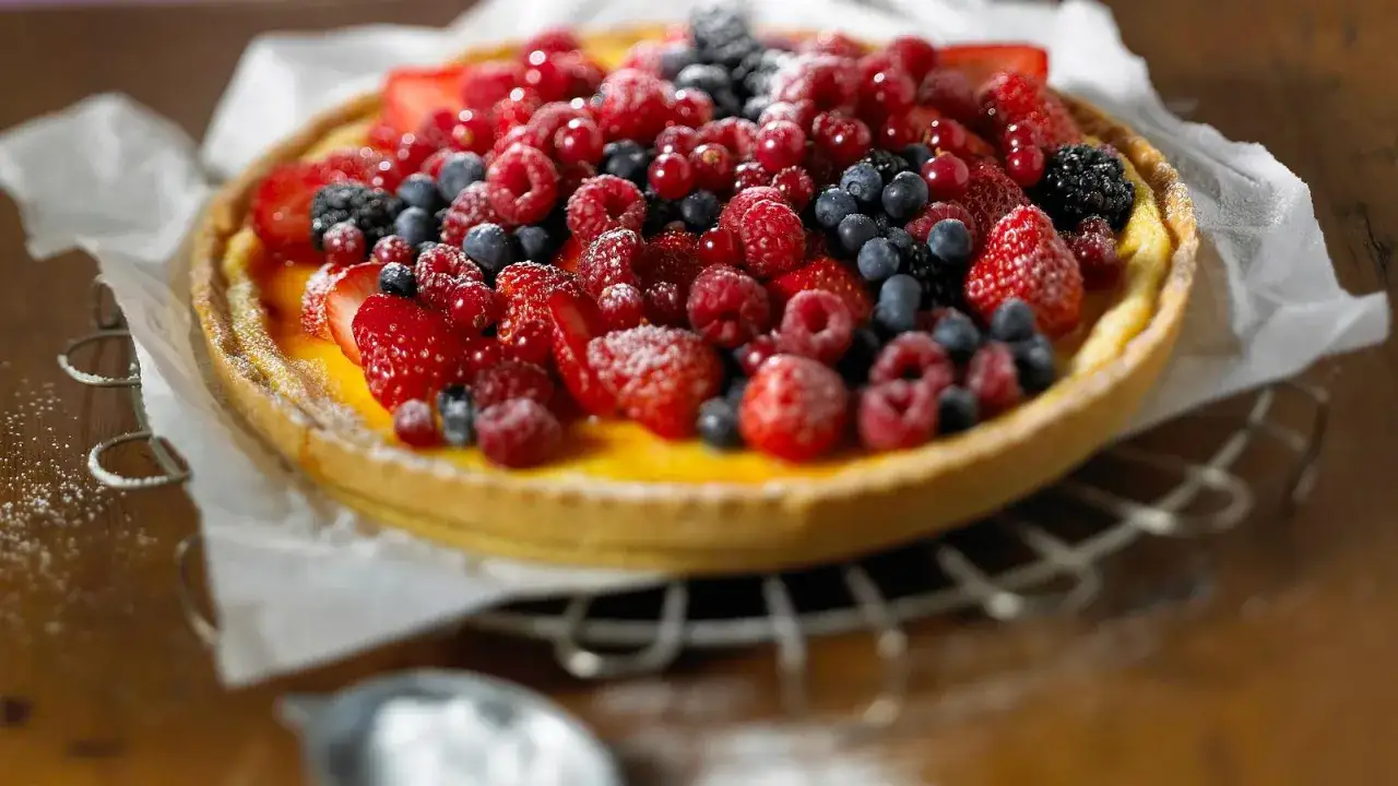Saftige vanille tartelettes, &uuml;berladen mit frischen Beeren wie Erdbeeren, Himbeeren und Blaubeeren, best&auml;ubt mit Puderzucker.