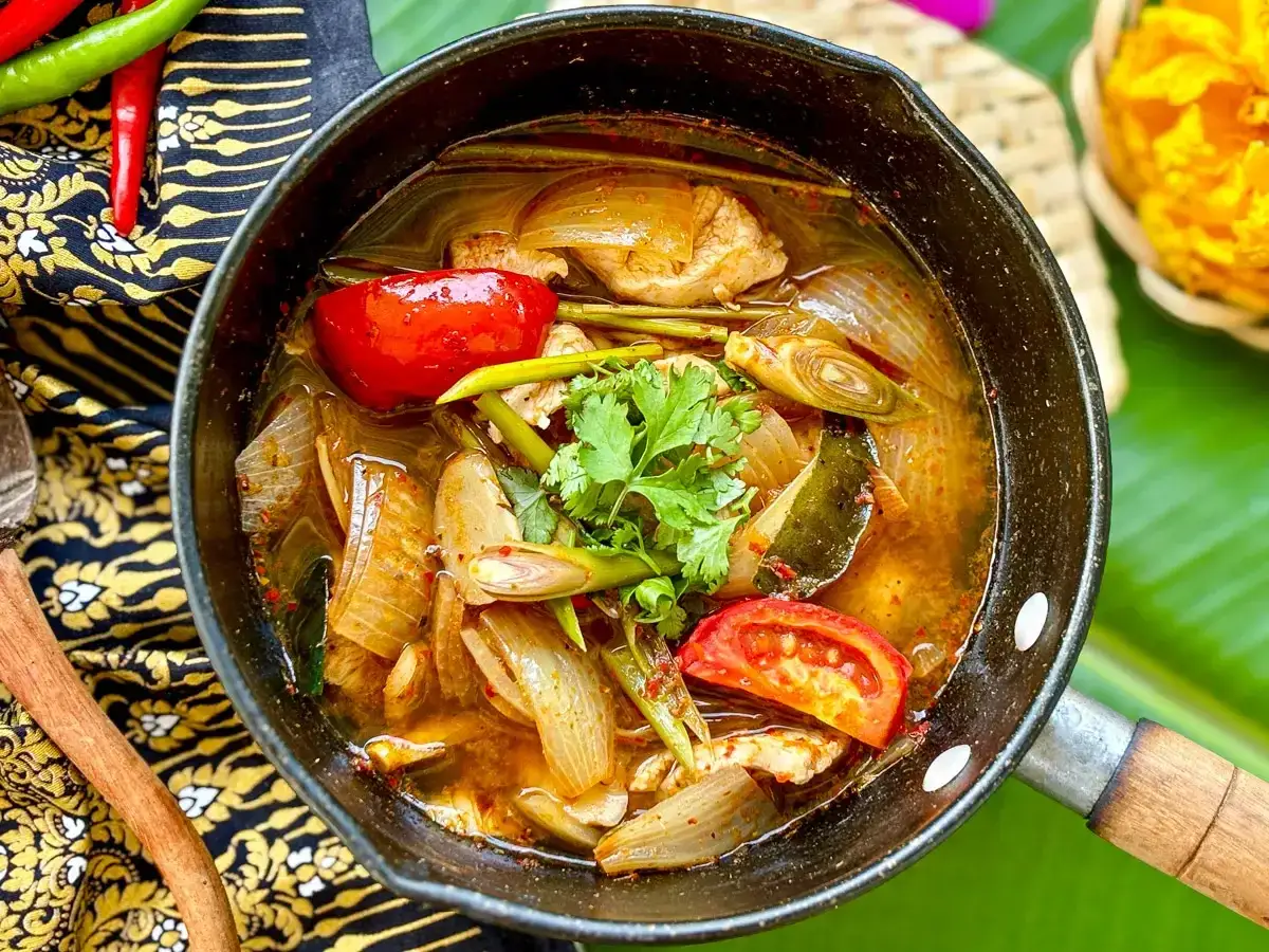 Eine dampfende Sch&uuml;ssel mit scharfer Thai Suppe, gef&uuml;llt mit H&uuml;hnchen, Tomaten, Zwiebeln und Zitronengras.
