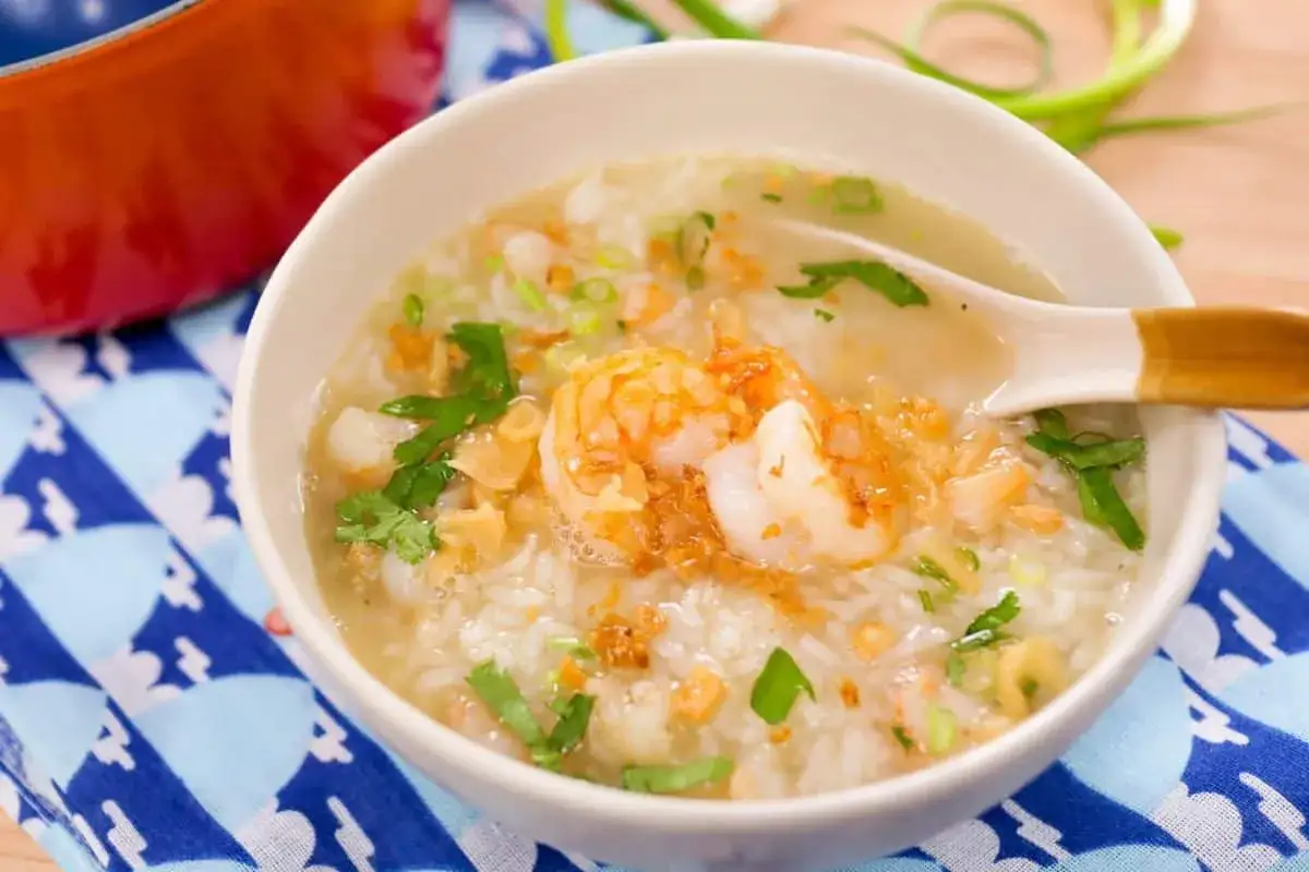 Khao tom, ein herzhafter Reisbrei mit Garnelen, garniert mit Fr&uuml;hlingszwiebeln und Koriander, serviert in einer Sch&uuml;ssel.