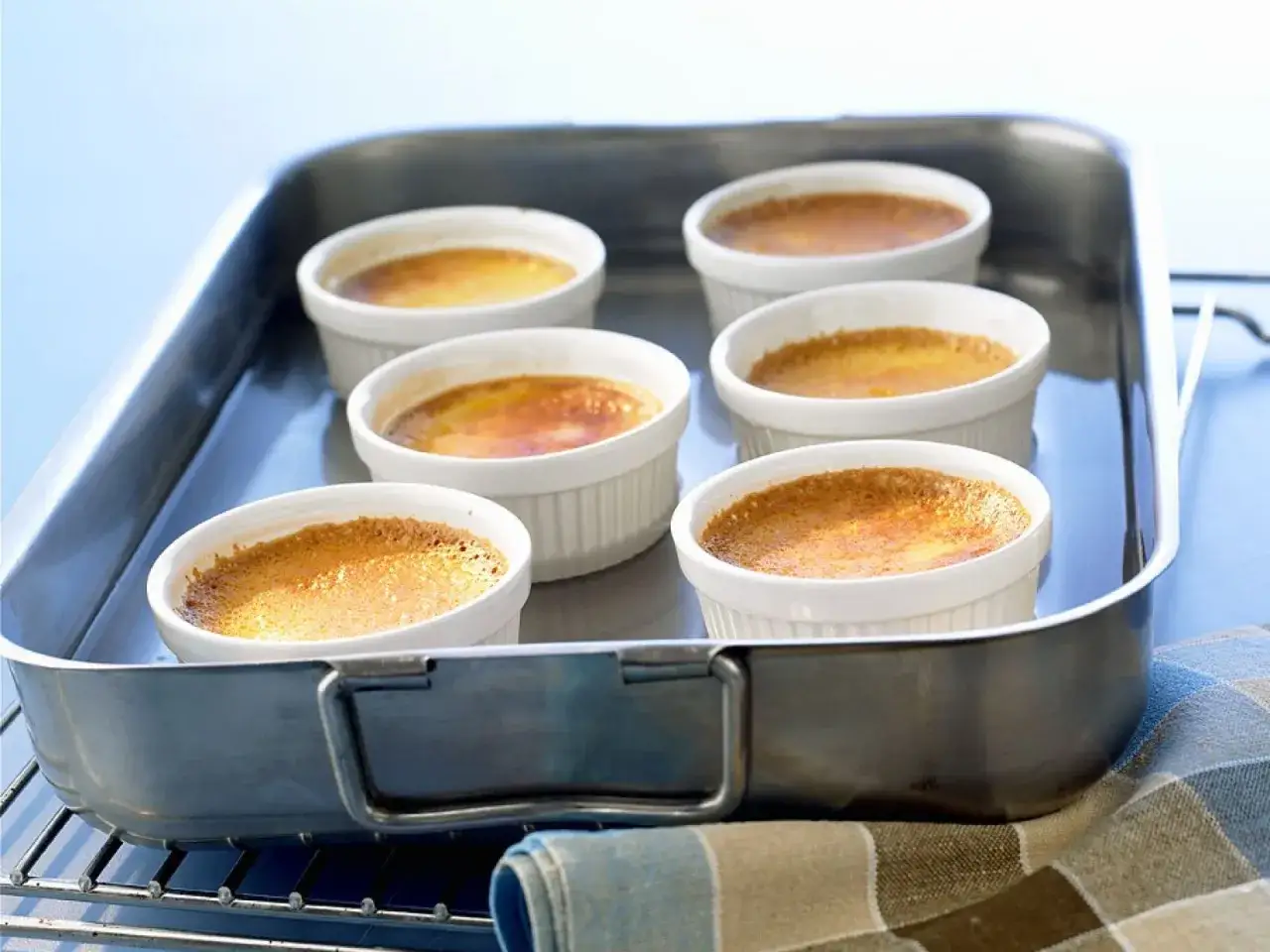 Sechs kleine, wei&szlig;e F&ouml;rmchen mit karamellisiertem Flan Pudding stehen in einer Metallschale.