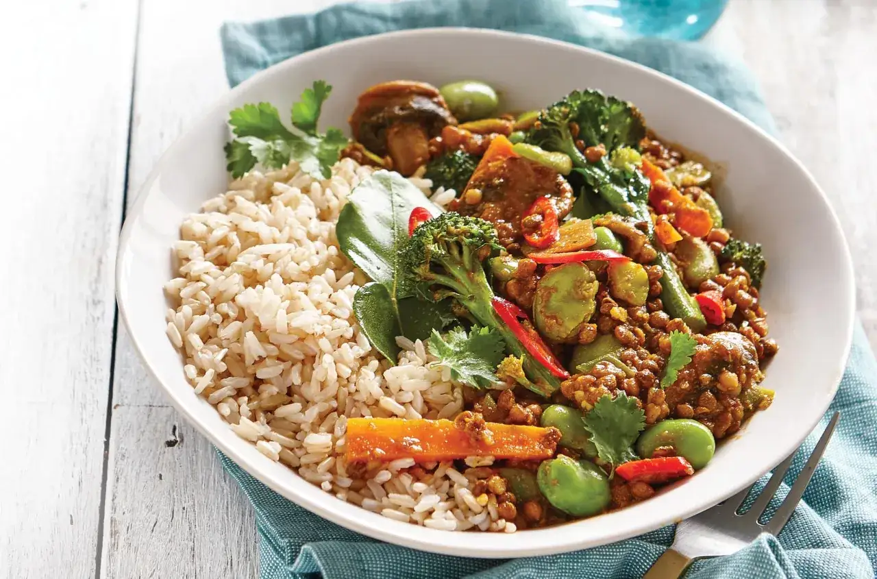 Ein k&ouml;stliches veganes Curry mit braunem Reis, Brokkoli, Karotten und gr&uuml;nen Bohnen, garniert mit frischem Koriander.
