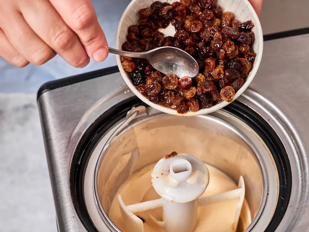 H&auml;nde geben Rosinen in eine Eismaschine f&uuml;r ein Malaga Eis Rezept.