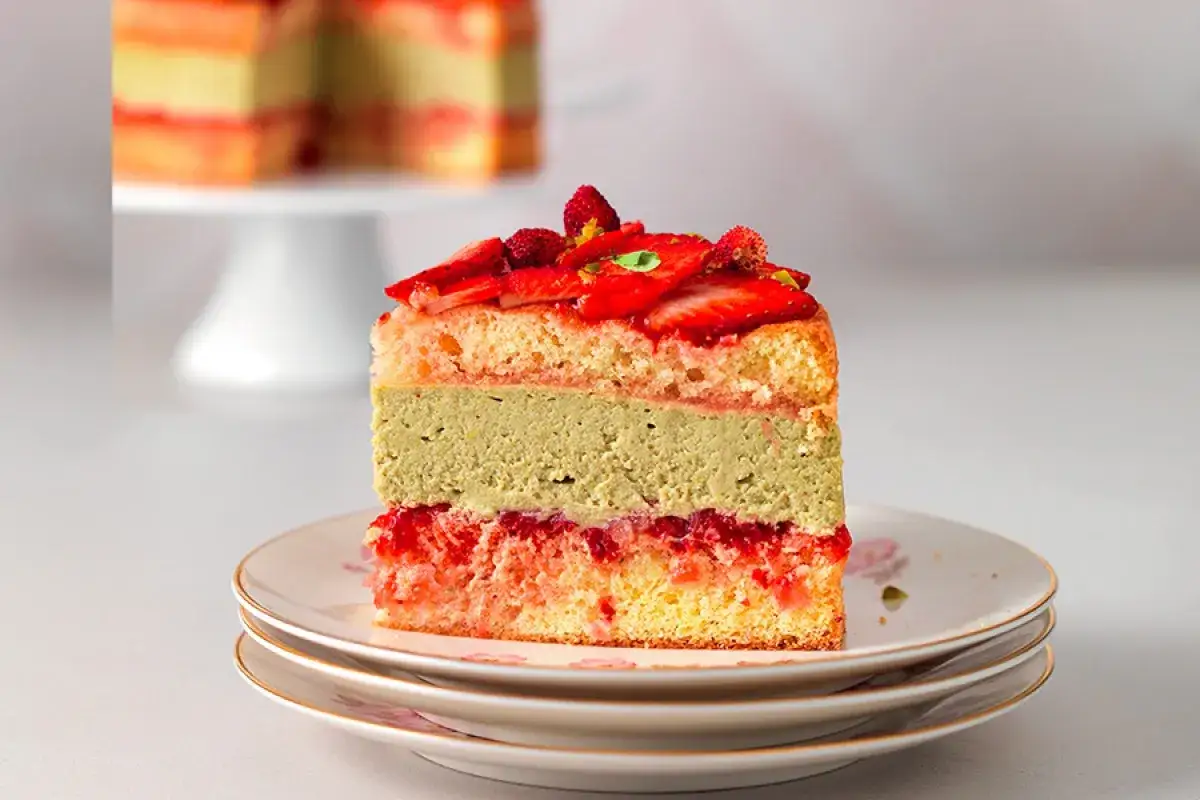 Ein St&uuml;ck Torte mit Erdbeeren und cremiger Pistazien Mousse, geschichtet auf Biskuit.