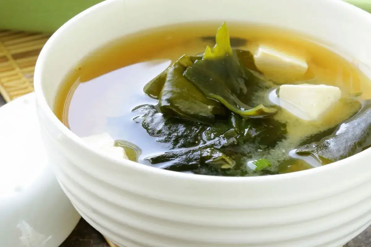 Eine Sch&uuml;ssel mit Seidentofu-Suppe, gef&uuml;llt mit zarten Tofuw&uuml;rfeln und dunklem Seetang in einer klaren Br&uuml;he.