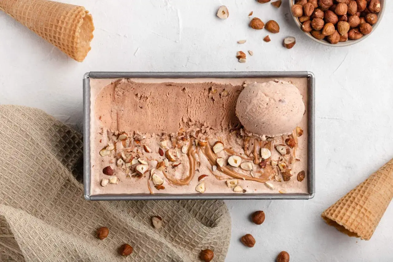 Schmackhaftes Haselnusseis selber machen: Ein Beh&auml;lter mit cremigem Eis, garniert mit gehackten Haseln&uuml;ssen und einem L&ouml;ffel Eis.