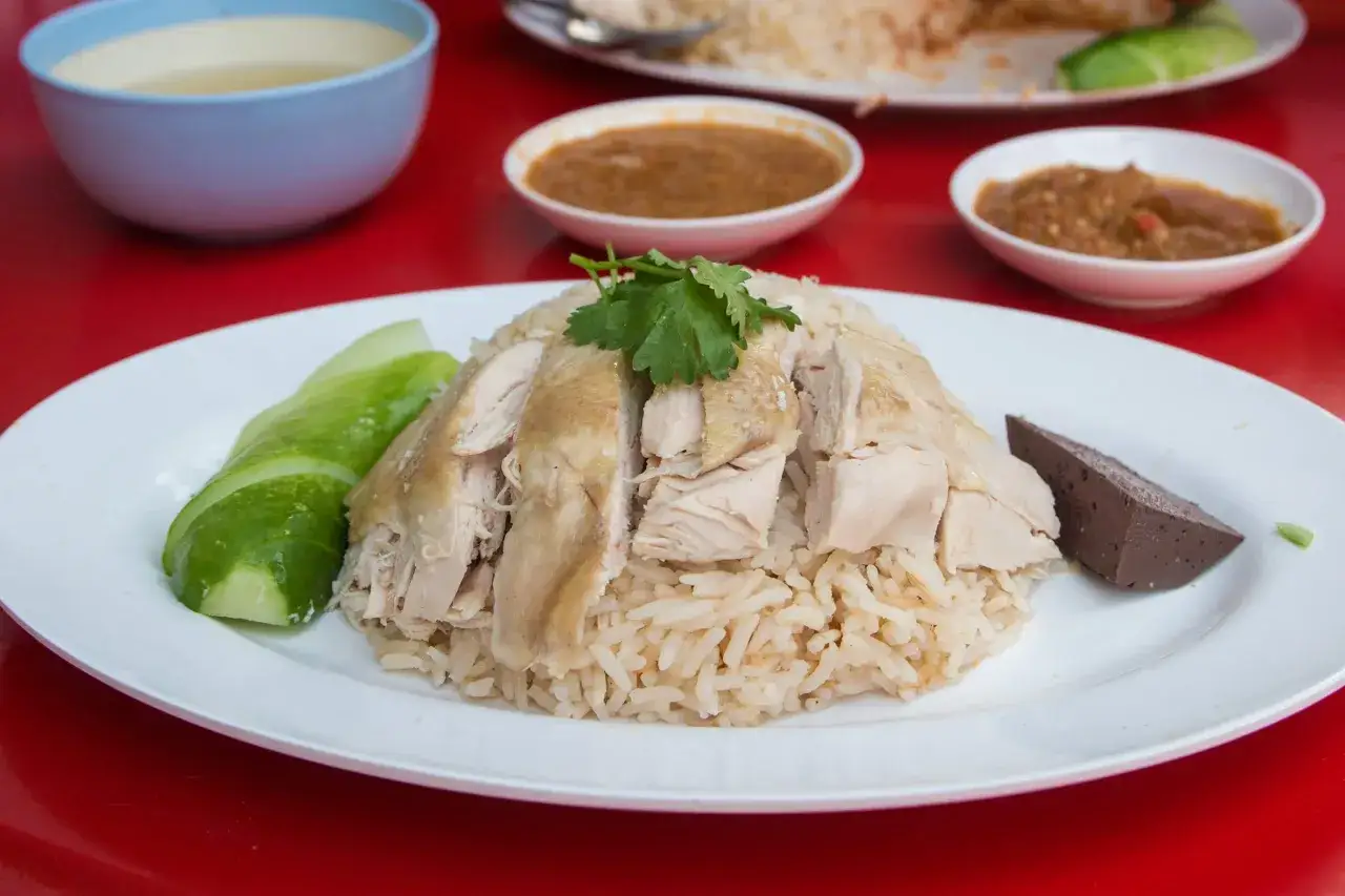 Khao Man Gai: zartes H&auml;hnchen auf duftendem Reis, garniert mit Gurkenscheiben und Koriander. Dazu gibt es Saucen und eine Blutwurstscheibe.